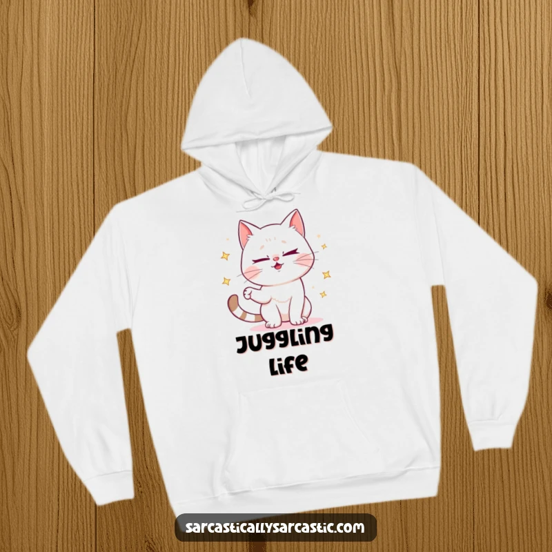 Funny hoodie featuring a mischievous cat winking and juggling sparkly items, perfect for cozy, playful moments.
